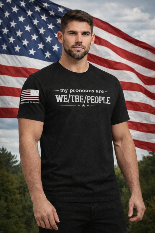 Man wearing a black t-shirt with 'my pronouns are WE/THE/PEOPLE' text in front of an American flag.