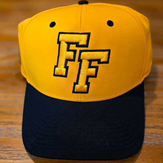 Gold cap with a black bill, black button and black eyelets with embroidered FF logo in gold outlined in black.  Cap is sitting on a wooden surface