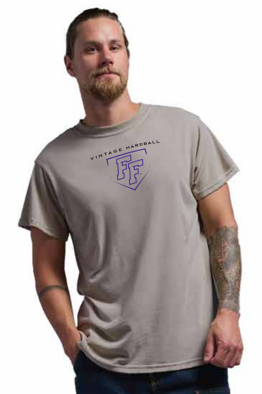 A man wearing a desert colored short-sleeve t-shirt with a graphic on the chest that reads 'VINTAGE HARDBALL' in blcak letters and features a purple baseball plate-shaped 'FF' logo underneath.