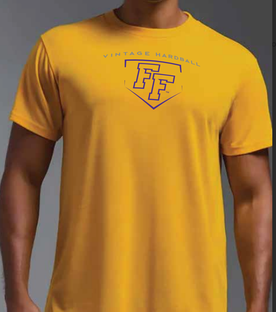 A man wearing a gold colored short-sleeve t-shirt with a graphic on the chest that reads 'VINTAGE HARDBALL' in gray letters and features a purple baseball plate-shaped 'FF' logo underneath.